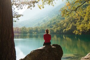 Person sitting calmly by a peaceful lake, symbolizing the tranquility and relaxation achieved through hypnotherapy for anxiety relief.